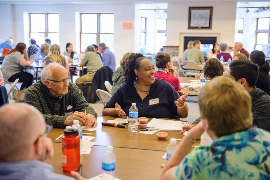 A group of attendees in a meeting room, sitting around tables